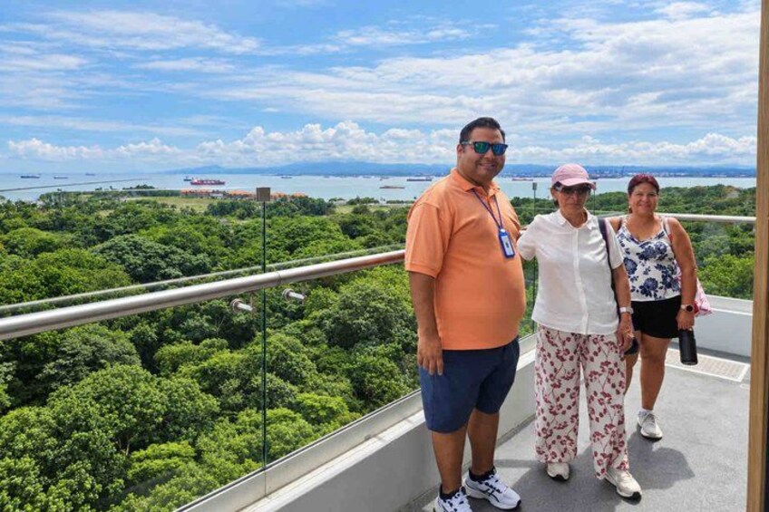 A group of people on a balcony overlooking a coastal landscape with dense greenery and a view of the sea. 2