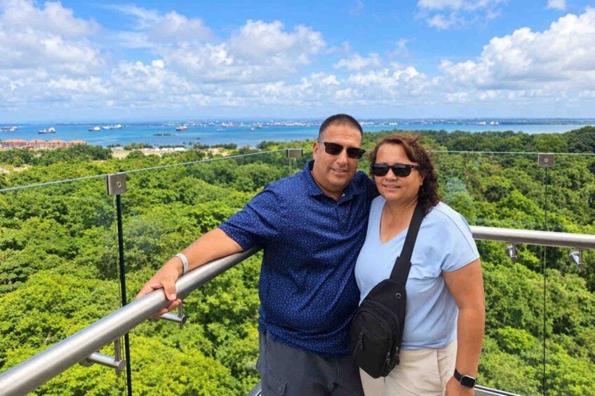 A couple standing on a balcony with a view of a lush green landscape and the ocean in the distance. 3