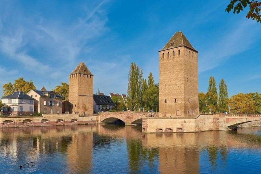 A river with two towers, a bridge, and buildings along the riverbank. 3