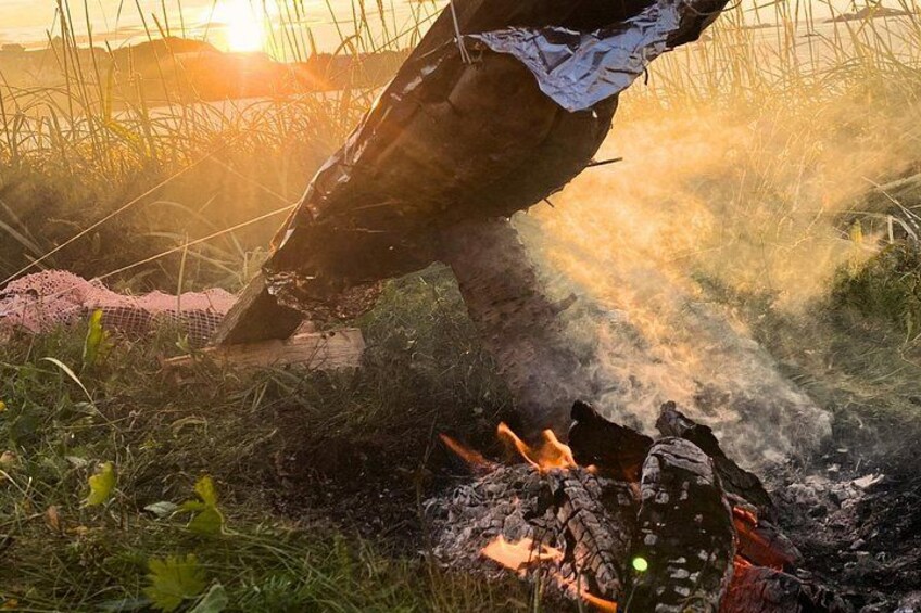 A campfire with logs and a tarp in a grassy area with a sunset in the background. 2