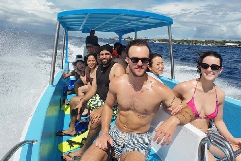 A group of people on a boat with a blue canopy, water in the background, and a distant shoreline. 3