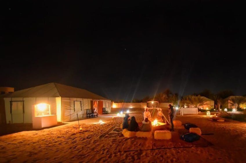 A desert camp at night with tents, a campfire, and people gathered around. 1