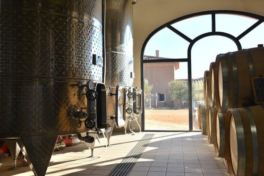 A winery interior with stainless steel tanks, wooden barrels, and a tiled floor. 1