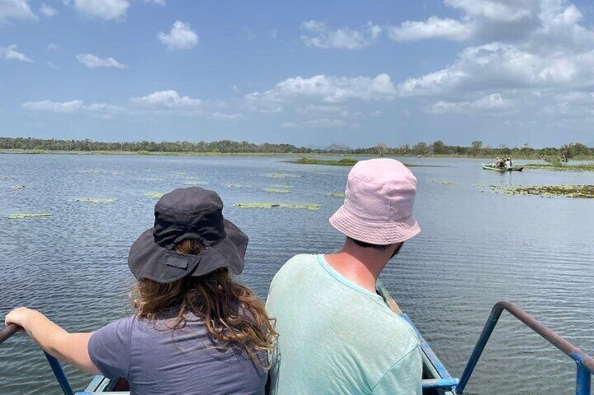Two people on a boat in a calm lake with lily pads and distant trees. 2