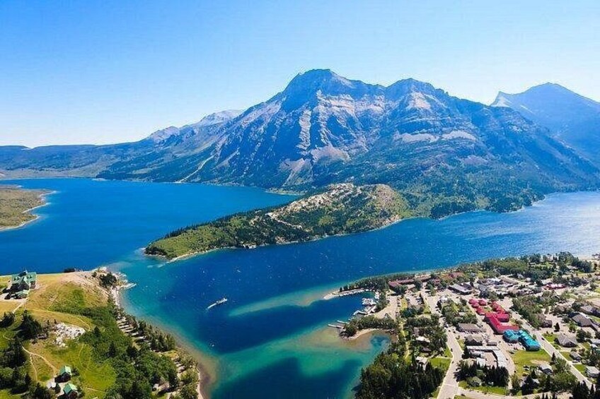 A lake surrounded by mountains, a small town, and clear skies. 1