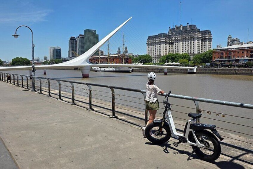 A person standing next to a white bicycle on a bridge with a cityscape in the background. 3