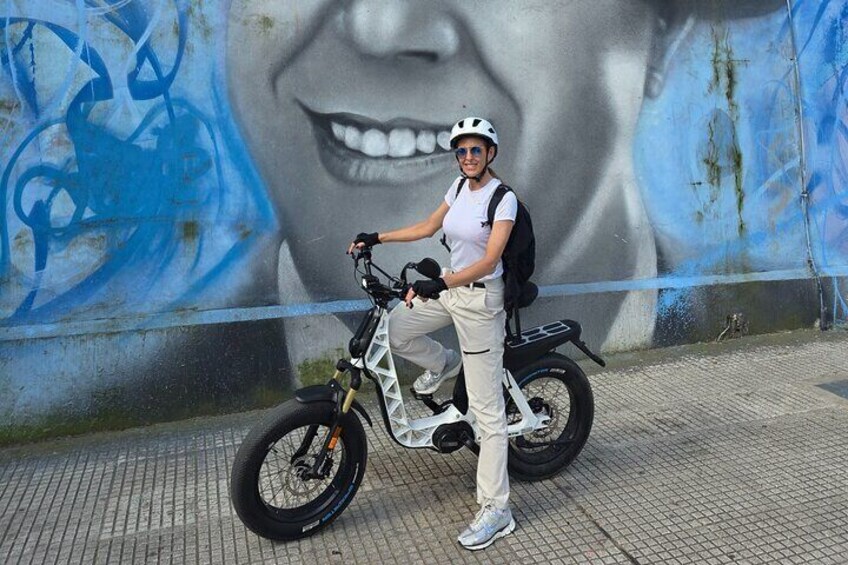 A person standing next to a white electric bike with a mural in the background. 5