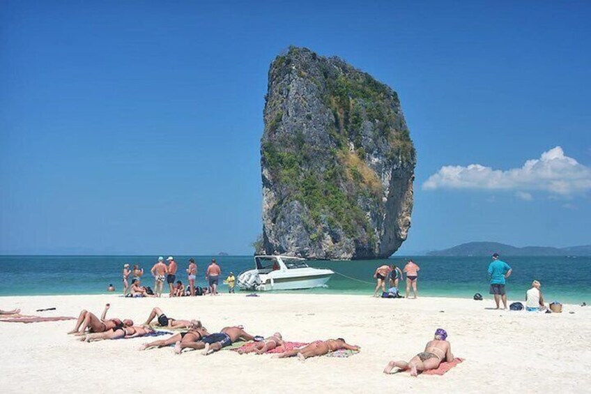 A beach with people sunbathing and a boat near a large rock formation. 4