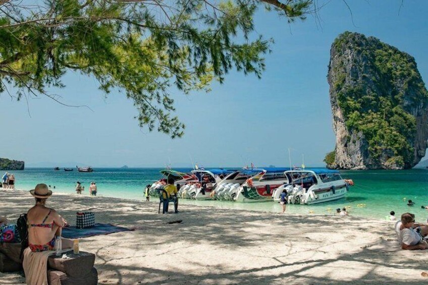 A beach with boats docked, people sunbathing, and a large rock formation in the background. 3