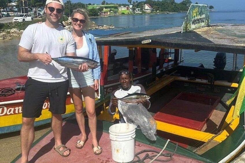 Un bateau avec des personnes tenant des poissons, une étendue d’eau et un quai en arrière-plan. 1