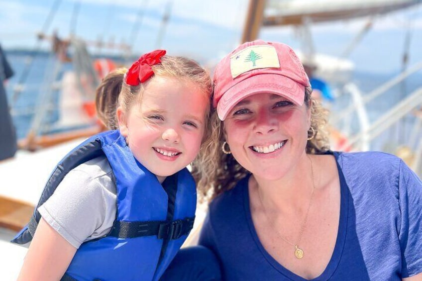 A person wearing a blue life jacket and a red cap with a green symbol, standing on a boat. 4