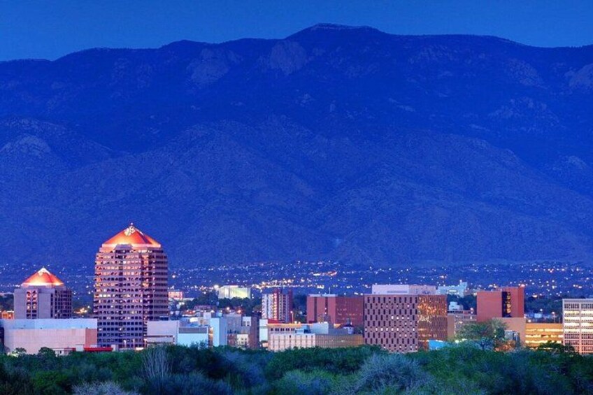 Un paisaje urbano al anochecer con edificios iluminados y montañas al fondo. 5