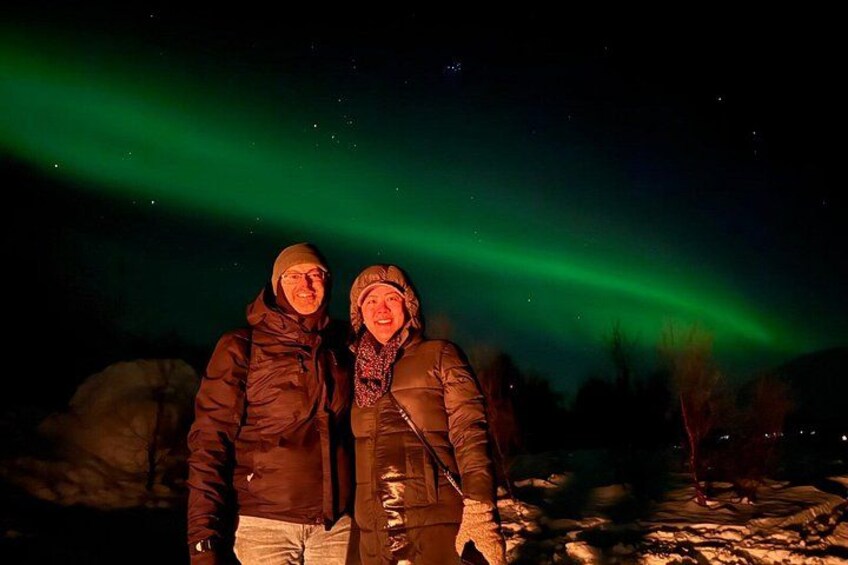 Twee personen staan in een besneeerd landschap onder een nachthemel met het noorderlicht. 1