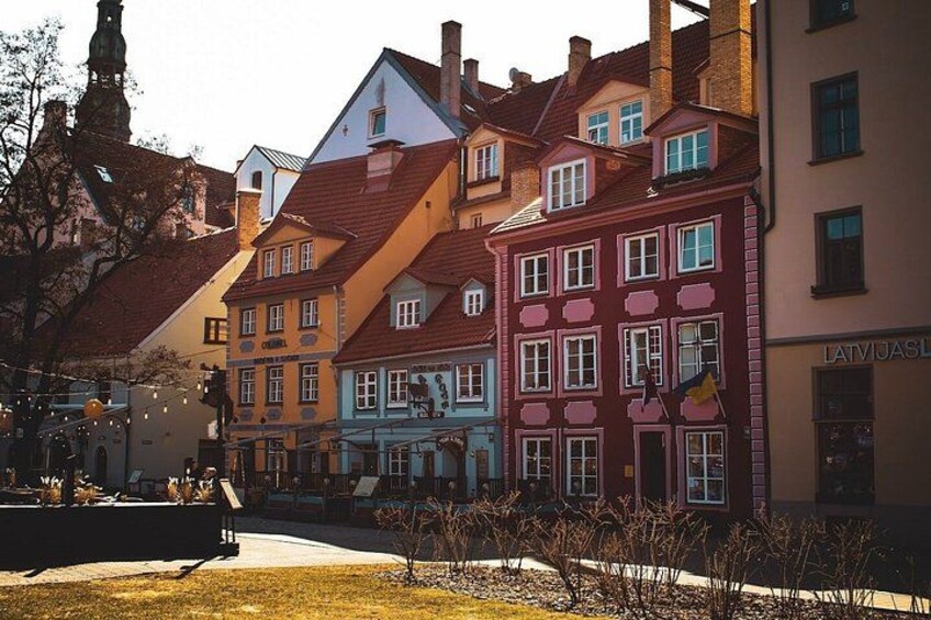 Une rue bordée de bâtiments aux couleurs vives, une statue et une enseigne indiquant « LETTONIE ». 3