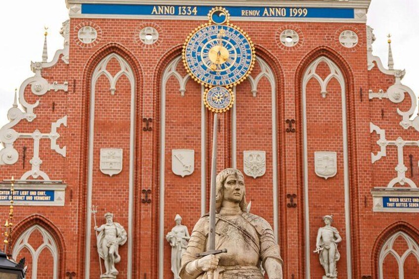 Ein roter Backsteinbau mit gotischen Bögen, einer großen Uhr und Statuen. 1