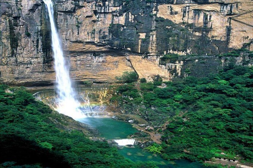 A waterfall cascading into a river surrounded by lush greenery and rocky cliffs. 2
