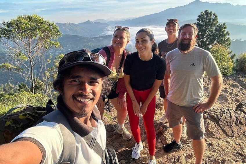 A group of people on a rocky mountain trail with trees and a distant view of a valley. 4