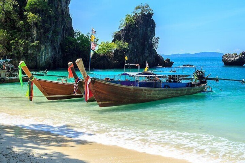 Two traditional wooden boats with outriggers docked at a beach with clear turquoise water and rocky cliffs in the background. 3