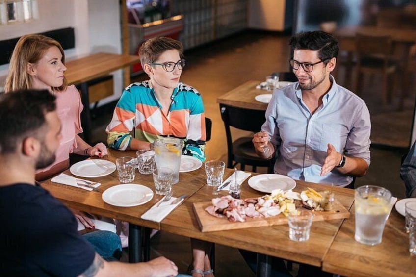 A group of people sitting around a wooden table in a restaurant, with plates of food and drinks. 1