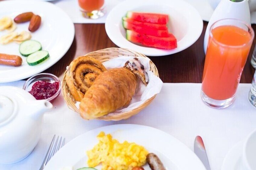 A breakfast setting with croissants, scrambled eggs, sausages, watermelon, and a glass of orange juice. 2