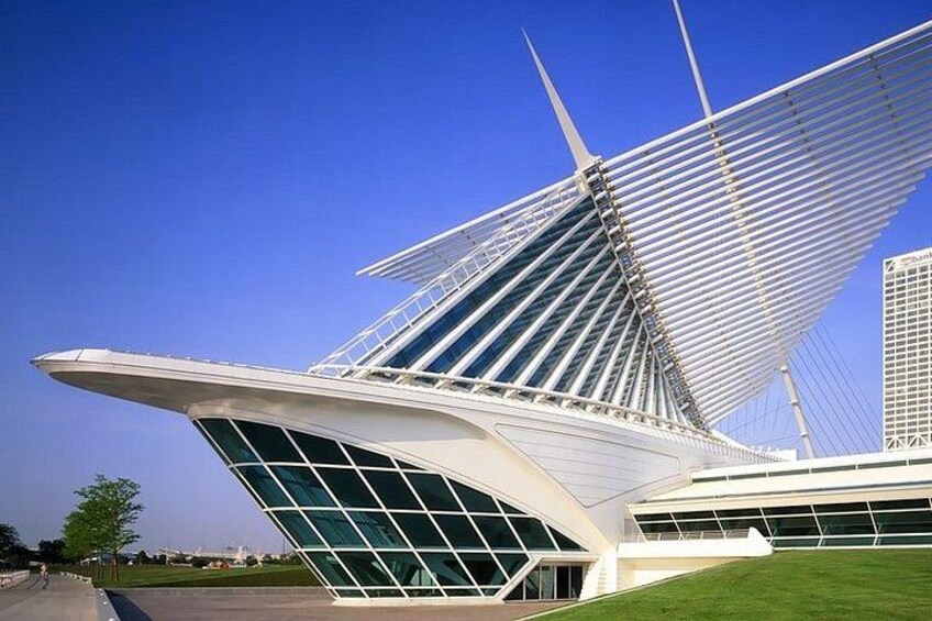 A modern architectural structure with a distinctive sail-like design, a glass facade, and a green lawn area. 5