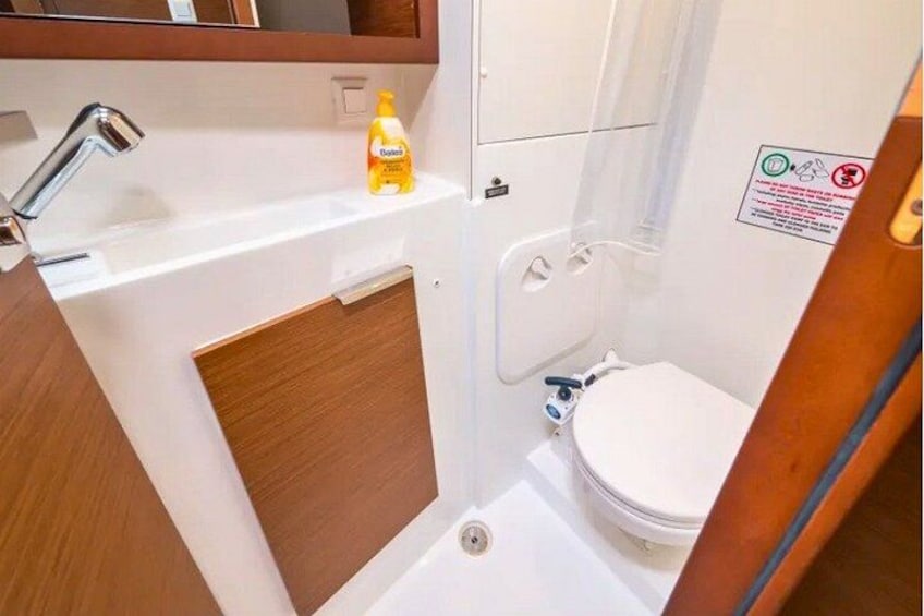 A compact bathroom with a white sink, a bottle of hand soap, and a toilet. 2