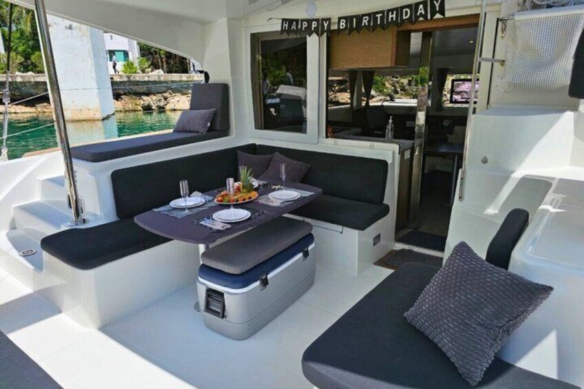 A boat's interior with a dining area, cushioned seating, and a birthday banner. 3