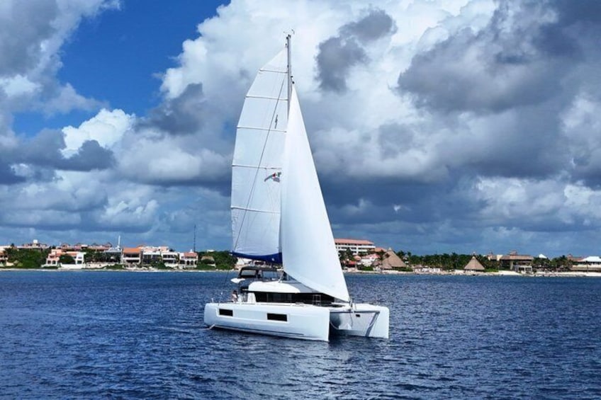 A white sailboat on calm water with a cloudy sky and a coastal town in the background. 4