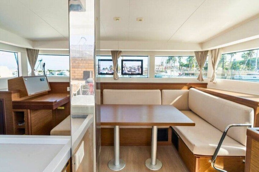 A boat interior with a wooden table, cushioned seating, and windows. 2