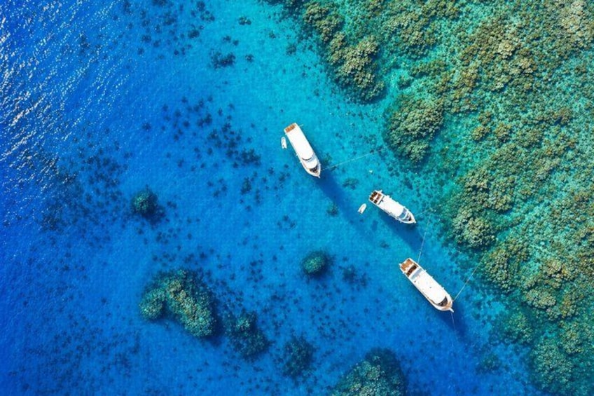 Vista aérea de un mar azul cristalino con arrecifes de coral y tres barcos anclados. 1