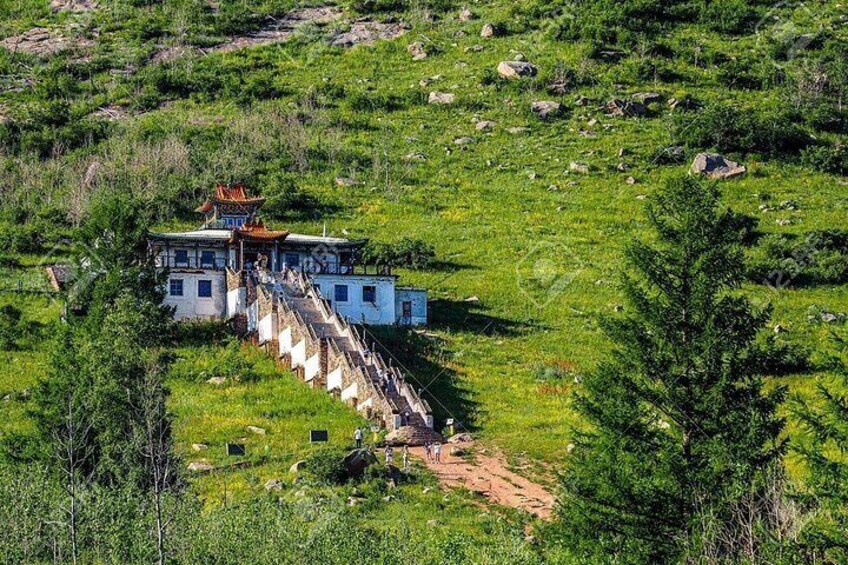 A traditional building with a staircase leading up to it, surrounded by greenery and rocks. 5