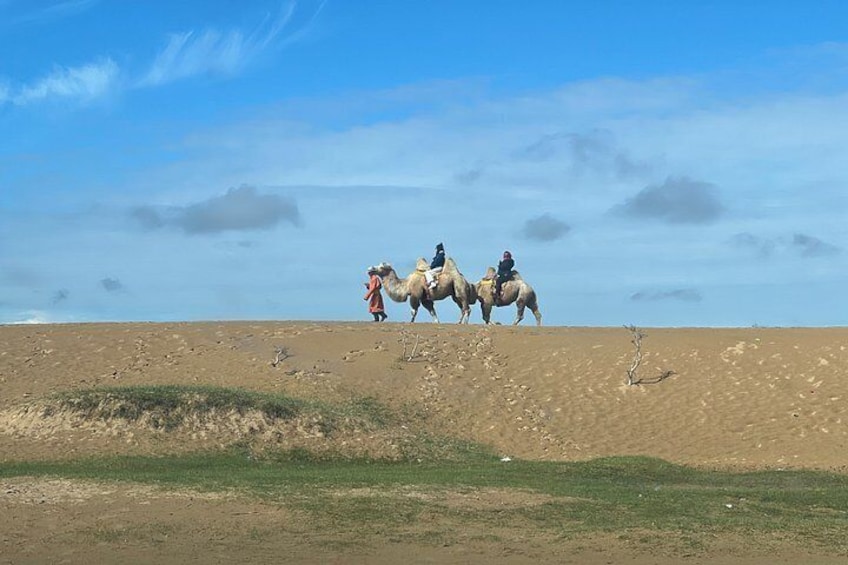 A desert landscape with a group of people riding camels. 3
