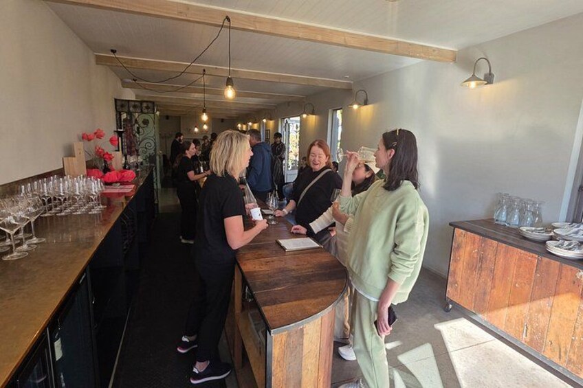 A bar area with wooden counters, glasses, and people standing around. 2