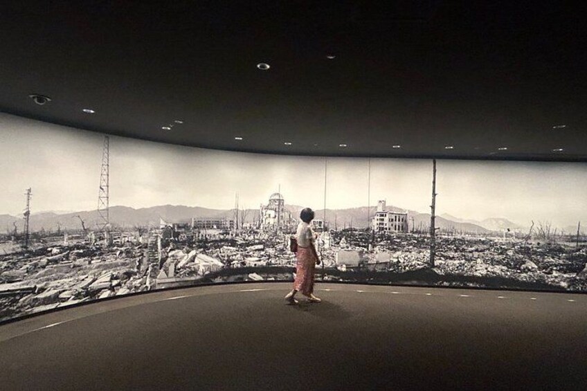 Eine Person steht auf einer gewölbten Plattform und genießt einen weiten Panoramablick auf eine Stadtlandschaft mit Gebäuden und Bergen. 5