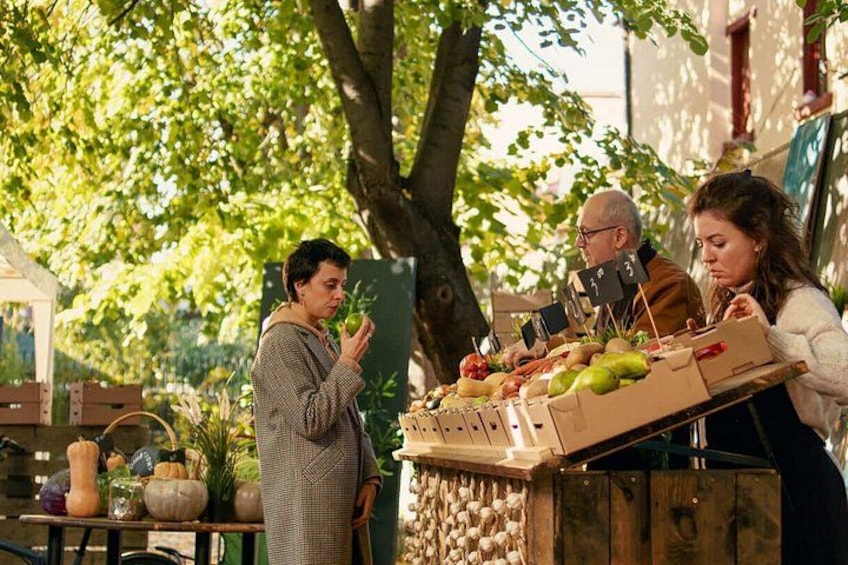 A person standing next to a table with various fruits and vegetables, a wooden fence, and trees in the background. 3