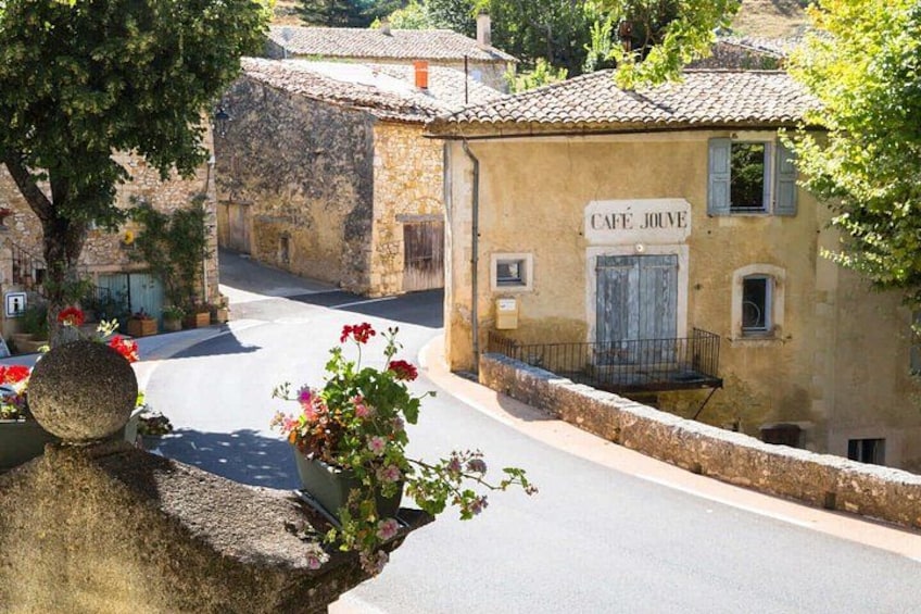 A quaint street with a café named 'Café Jouve,' stone buildings, and a stone wall with flowers. 2