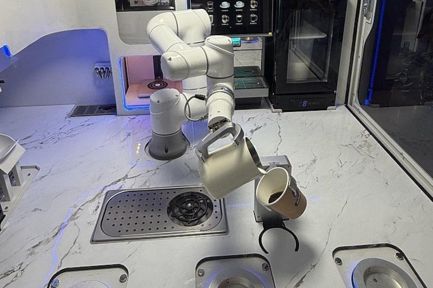 A robotic arm on a kitchen counter with a coffee machine and a microwave in the background. 4