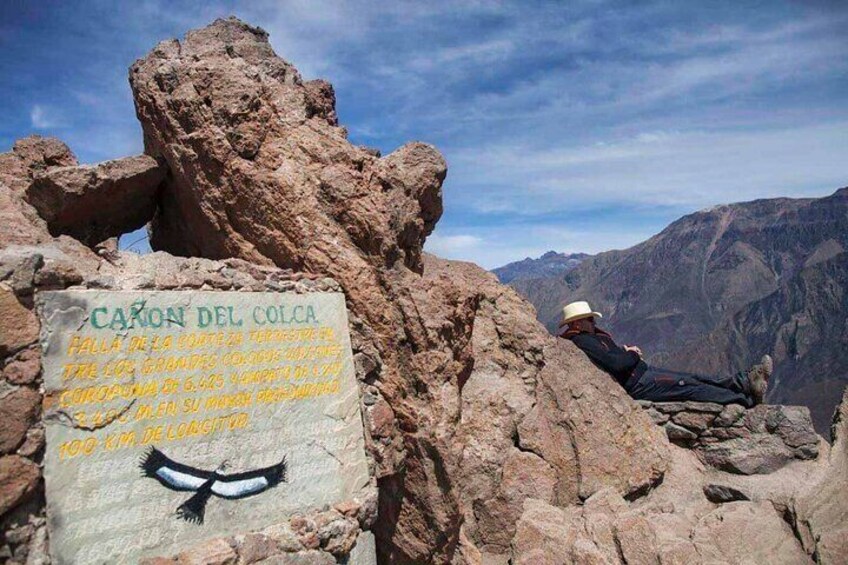 A rocky landscape with a sign reading "CAYON DEL COLCA" and a person sitting on a rock. 4
