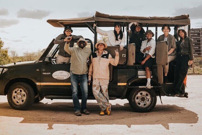 A group of people posing in front of a safari vehicle with a sign that reads "Main Camp." 1