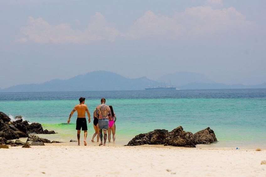 A beach with people walking, a ship in the distance, and mountains in the background. 2