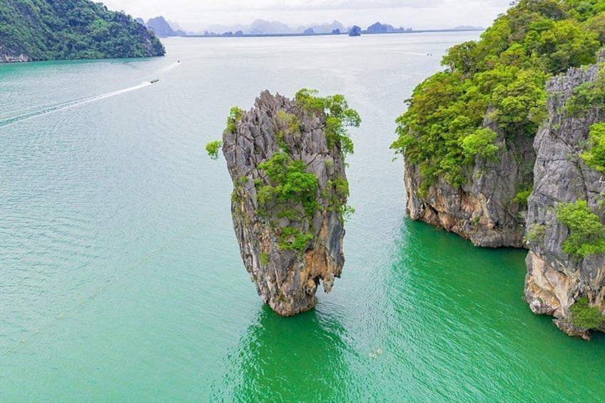 A large rock formation surrounded by turquoise water, with a boat visible in the distance. 1