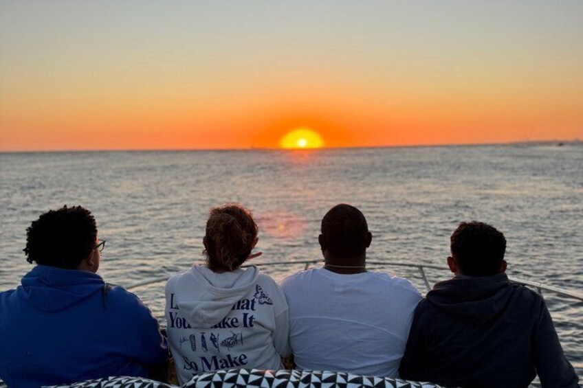 Three people on a boat watching a sunset over the ocean. 5