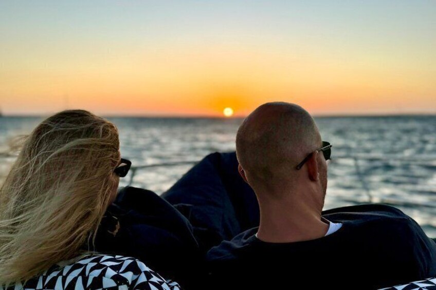 Two people sitting on a boat, facing the sunset over the ocean. 4