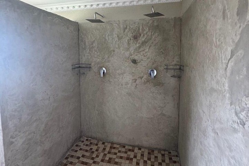 A shower with a checkered floor, a metal showerhead, and a wall-mounted faucet. 4