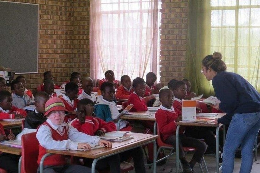 A classroom with students in red uniforms, a teacher assisting at the front, and a chalkboard. 5