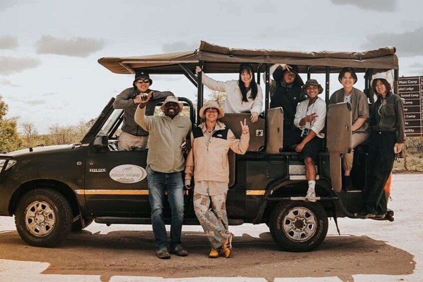A group of people posing with a safari vehicle in a desert-like environment. 3