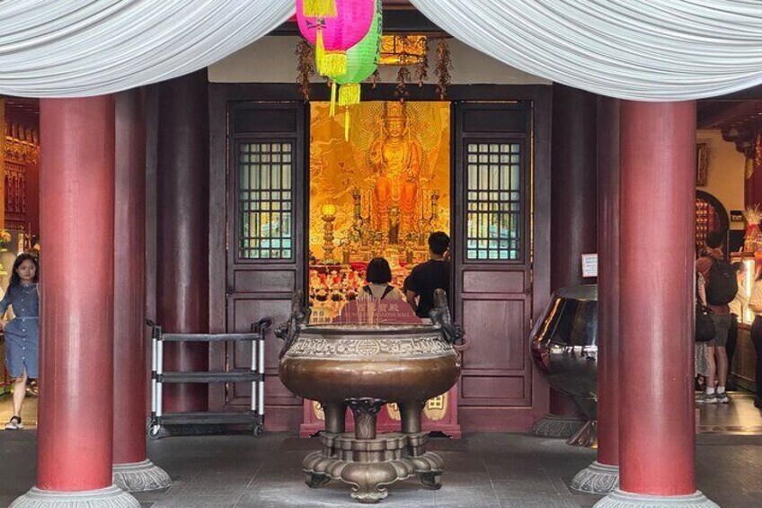 A temple entrance with a large ornate water container, red pillars, and a mural of a deity. 5