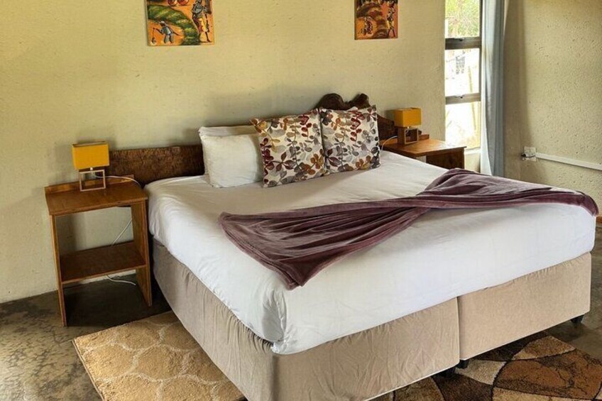 A neatly made bed with a purple throw, two pillows with a floral pattern, and a wooden nightstand with a lamp. 4