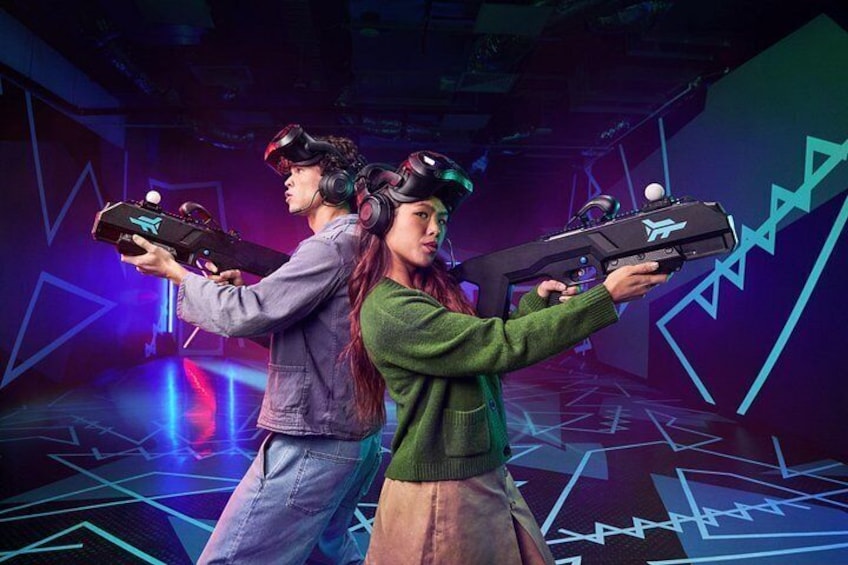 Two people wearing VR headsets holding VR controllers in a room with a geometric light pattern on the floor. 4
