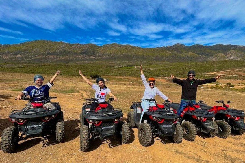 Four people on ATVs in a desert landscape with mountains in the background. 3